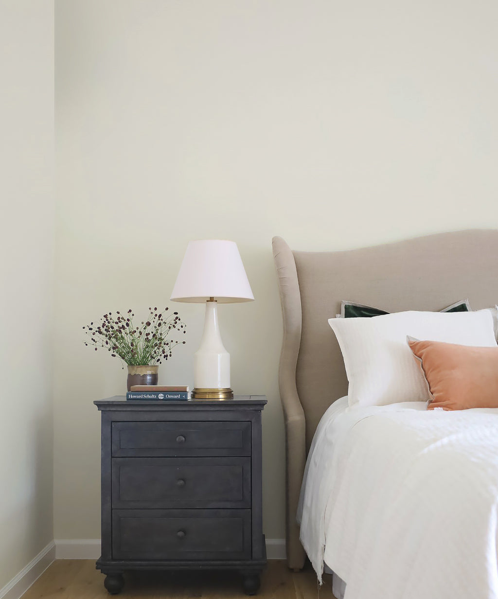 Bedroom with a nightstand featuring a lamp and decorative items, next to a bed with pillows.
