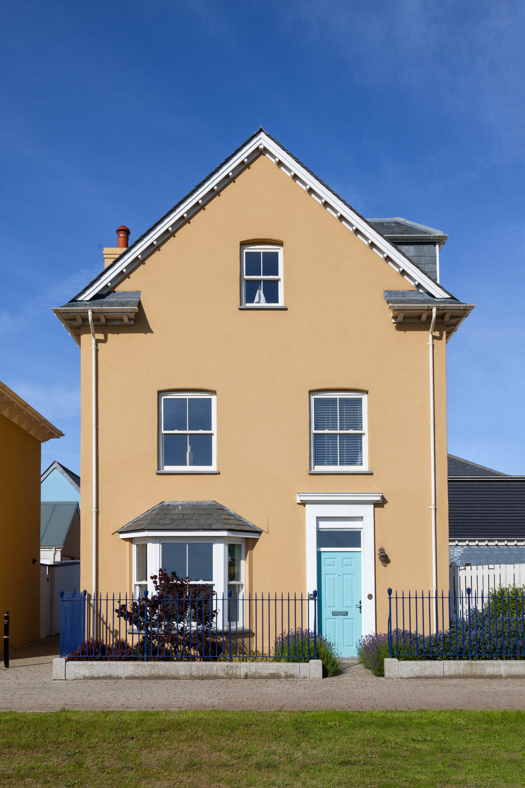 Two-story house with a light brown exterior and a blue door, set against a clear blue sky.