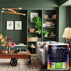 A styled living room interior with dark green walls, built-in shelving, a wooden coffee table, sofa, rug, and decorative plants. In the lower right foreground is a large canister label reading Fleetwood Colour Perfects, indicating the product being promoted.