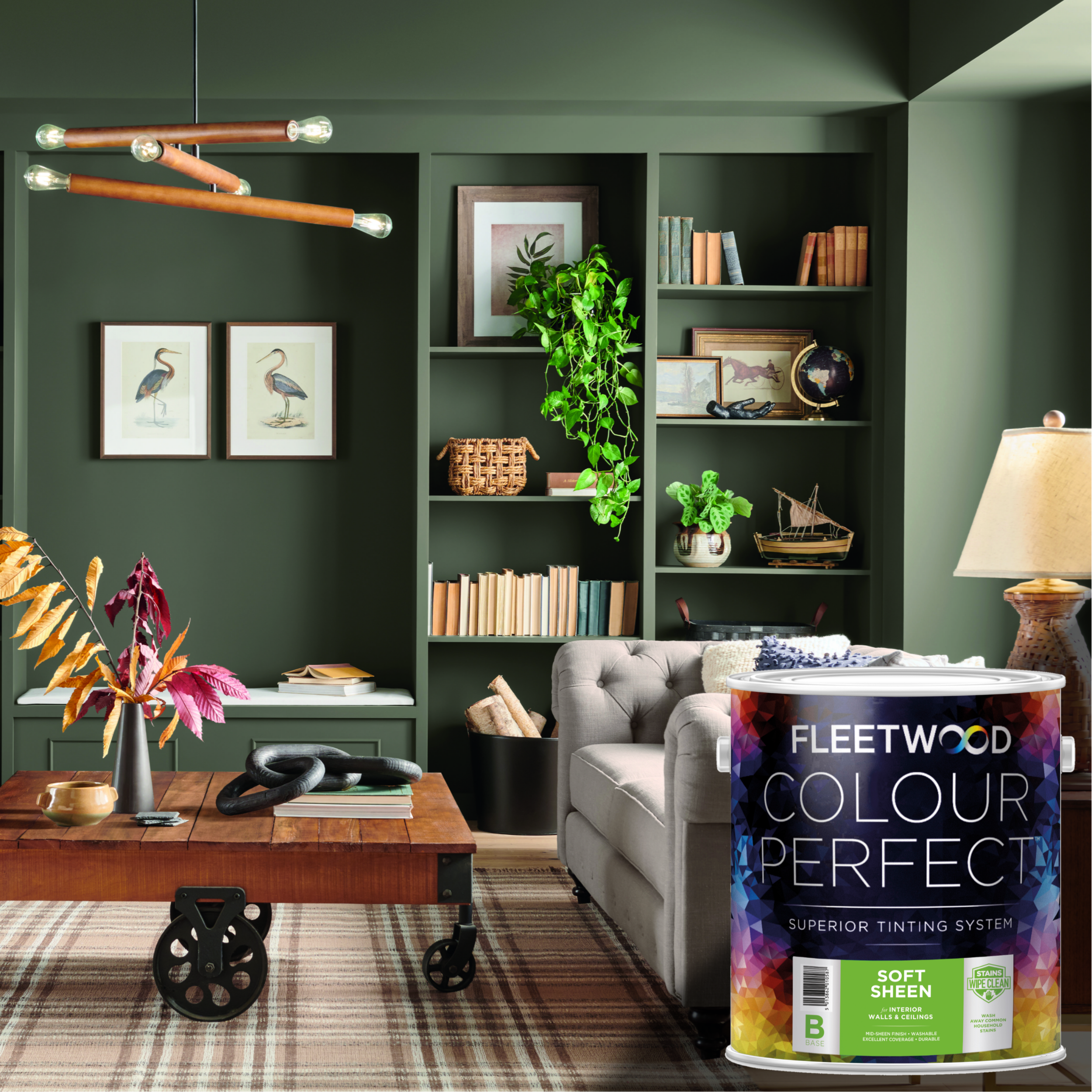A styled living room interior with dark green walls, built-in shelving, a wooden coffee table, sofa, rug, and decorative plants. In the lower right foreground is a large canister label reading Fleetwood Colour Perfects, indicating the product being promoted.