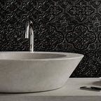 A modern bathroom scene featuring a large concrete vessel sink with a chrome faucet, set against a textured blue-gray embossed tile wall. A white teacup and saucer sit on the counter next to a smartphone.