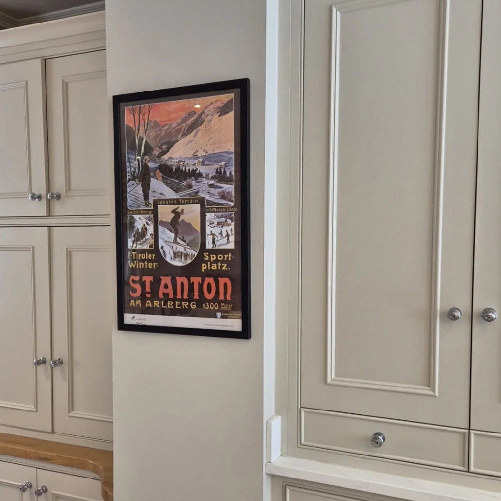 Framed St Anton poster on a wall between beige cabinets