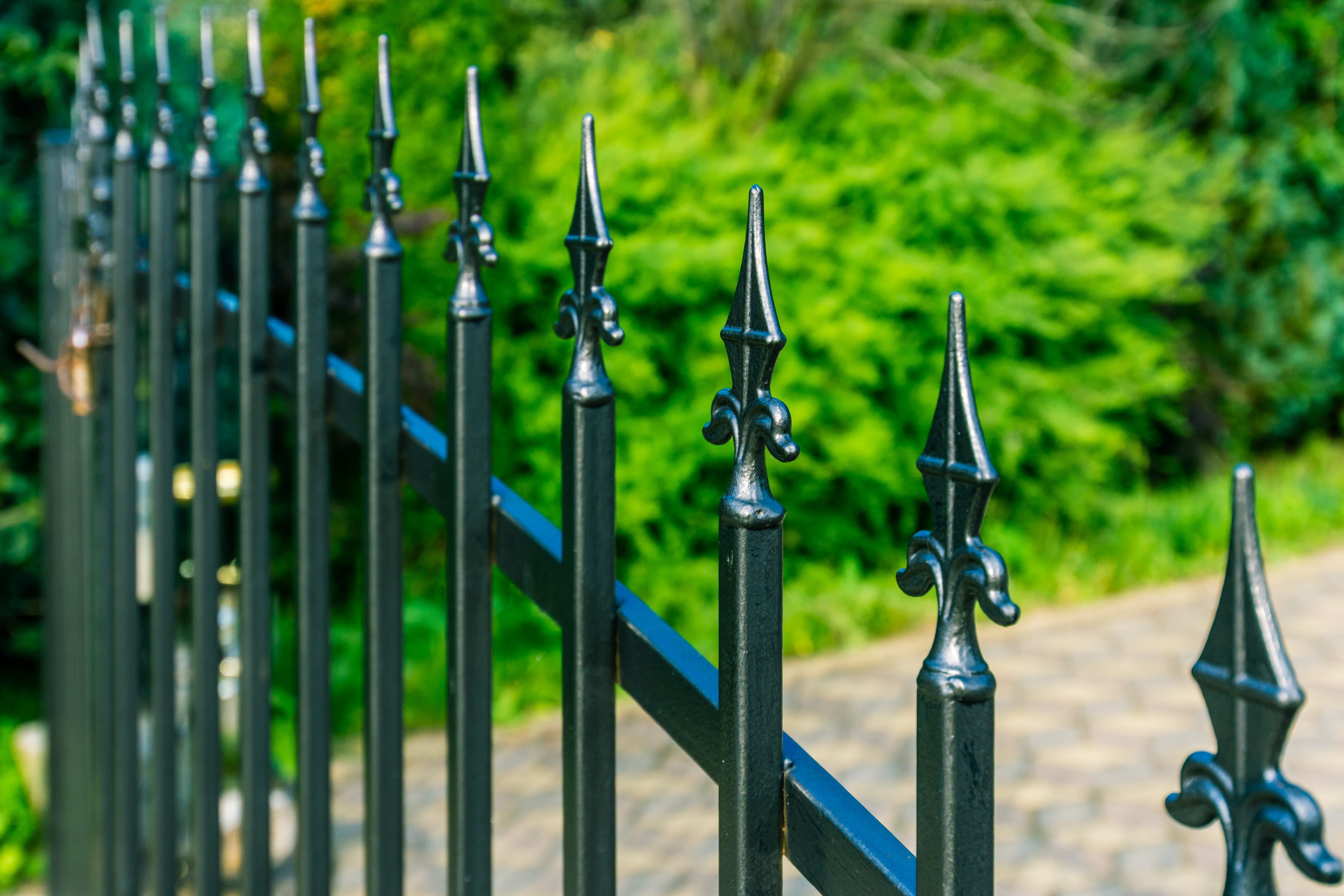 Black metal fence with decorative spikes against a blurred green background