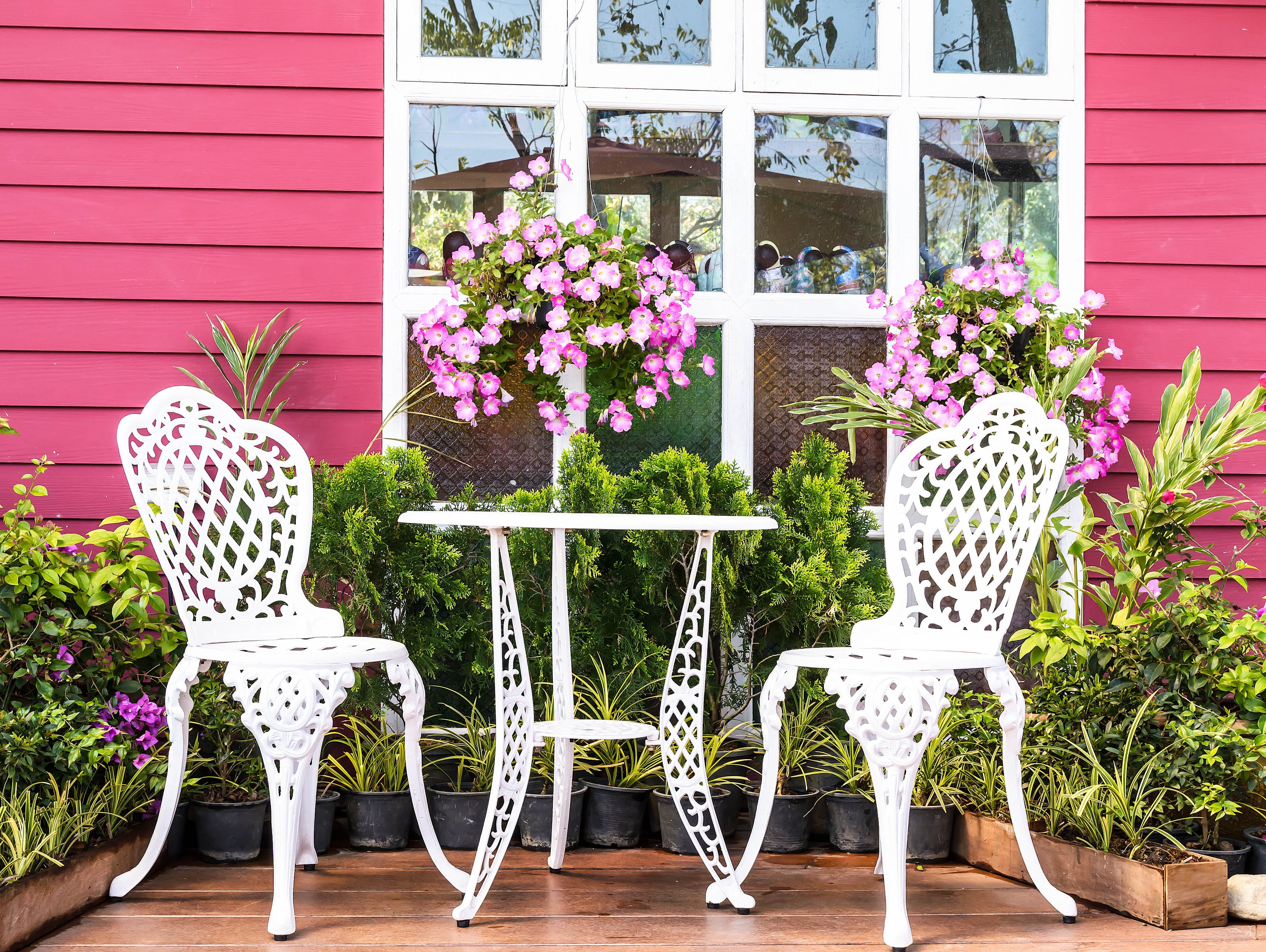 White metal chairs and table in front of a pink building with greenery and flowers.