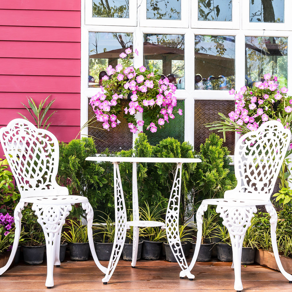 White metal chairs and table set on a wooden deck with pink wall and window in the background