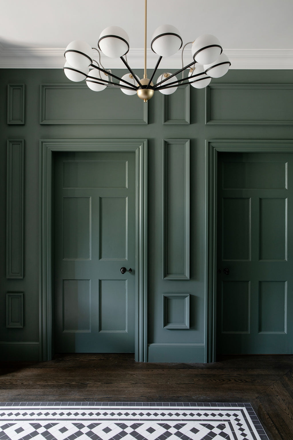 Modern chandelier hanging in a room with green paneled walls and a patterned rug.