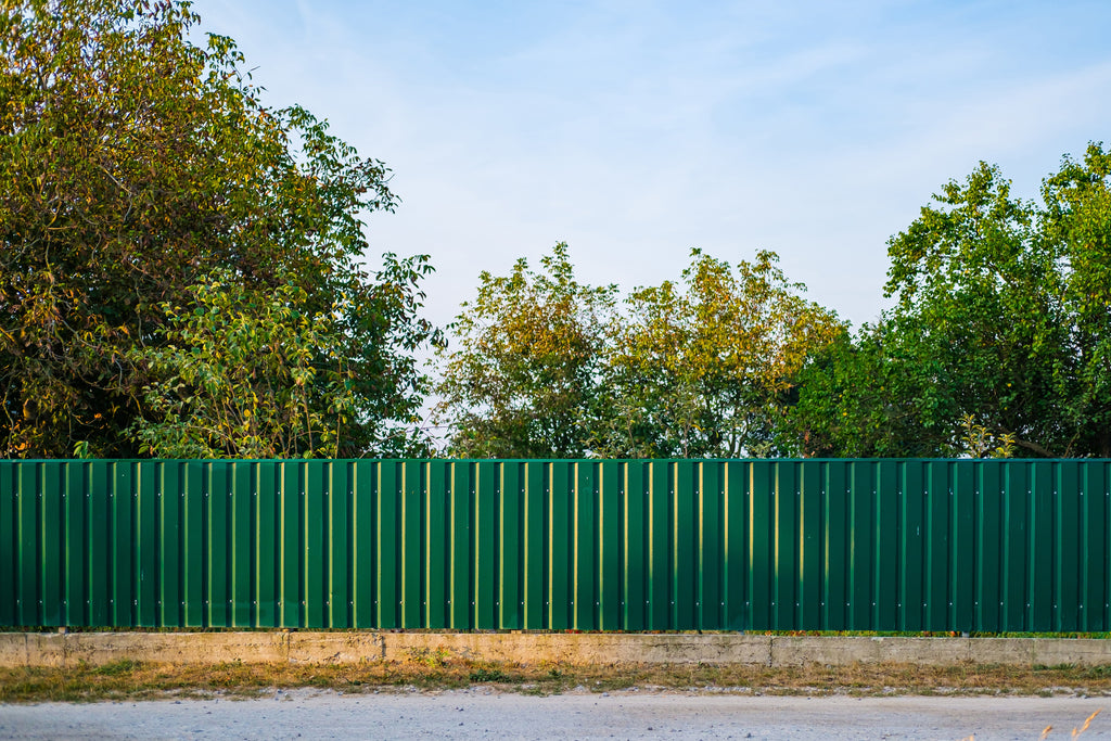 Green metal fence with trees in the background