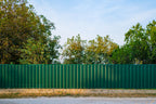 Green metal fence with trees in the background