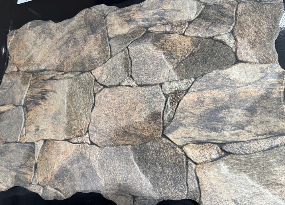 A stone-look decorative wall panel or tile sample with irregular faux-stone shapes in mixed gray, beige, brown, and charcoal tones, photographed against a black background.