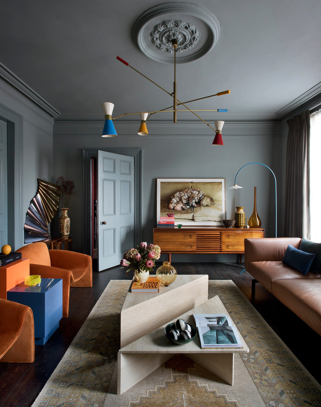 Modern living room with a colorful chandelier, gray walls, and a brown sofa.