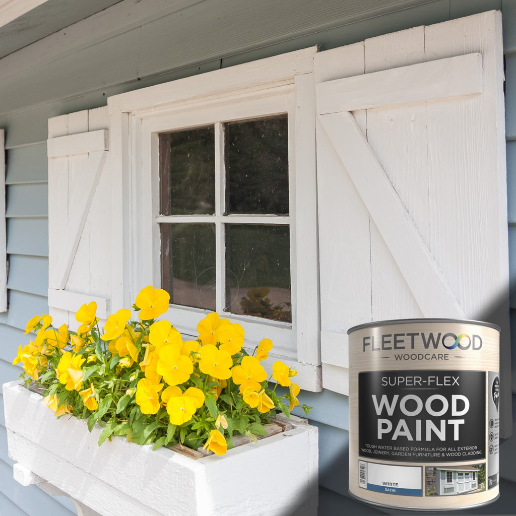 Fleetwood Woodcare Super-Flex Wood Paint can with a window box of yellow flowers in front of a house.